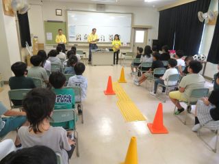 小牧市内小学校での福祉実践教室の様子。ガイドヘルプボランティアが子どもたちに点字ブロックや白杖について教えている。